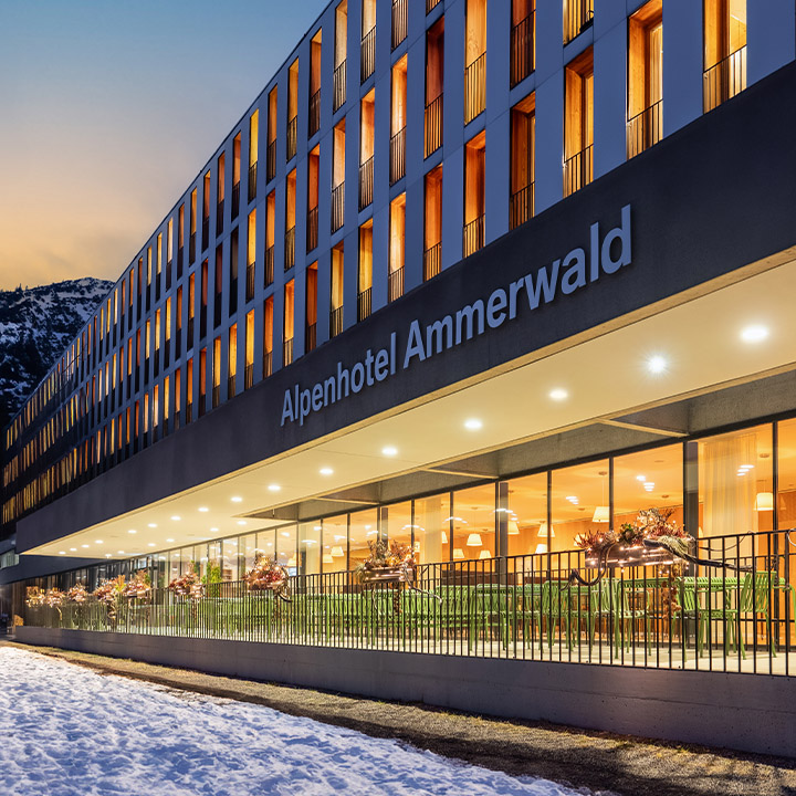 Terasse des Alpenhotel Ammerwald bei Dämmerung mit warmer Beleuchtung aus dem Hotel.