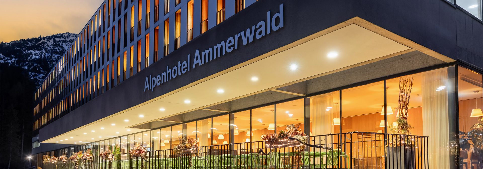 Terasse des Alpenhotel Ammerwald bei Dämmerung mit warmer Beleuchtung aus dem Hotel.