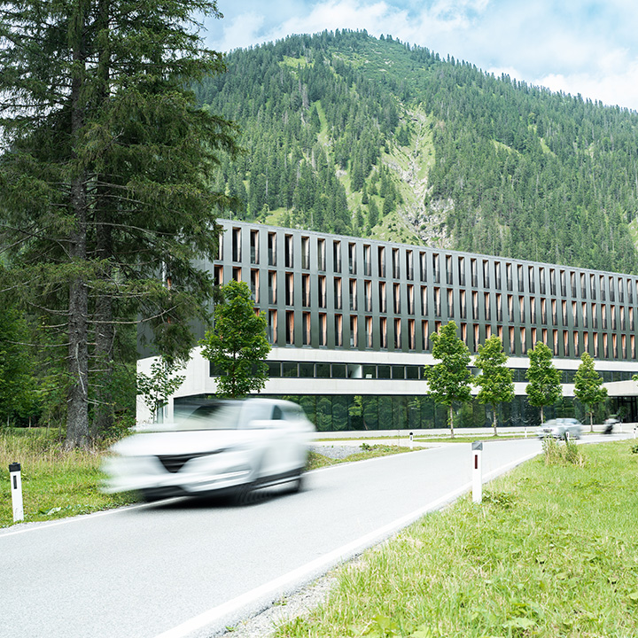 Das Alpenhotel Ammerwald mit einem Berg im Hintergrund und davor eine Straße, auf der sich ein weißes Fahrzeug bewegt.