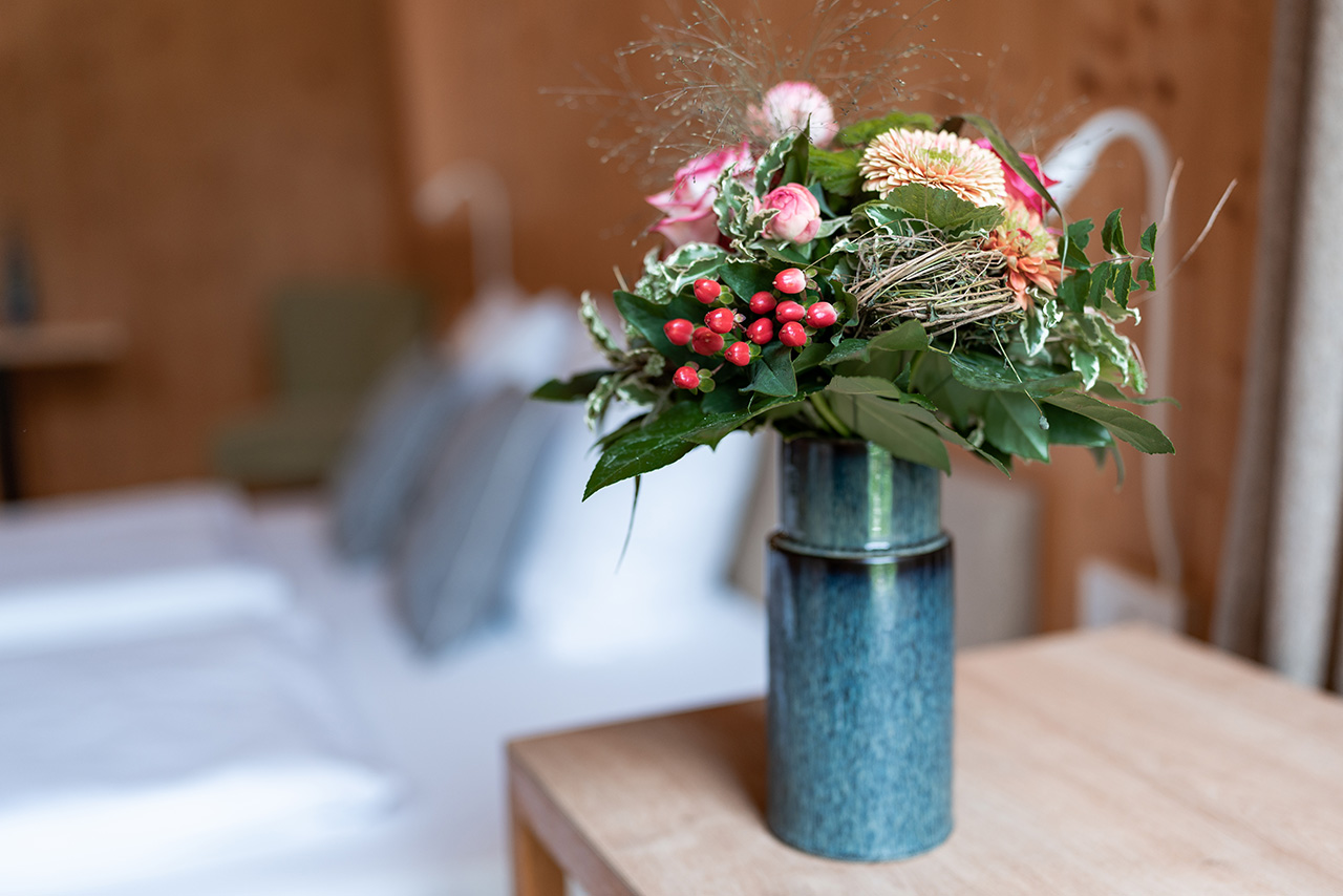 Bunter Blumenstrauß in einer blauen Vase auf einem Holztisch.