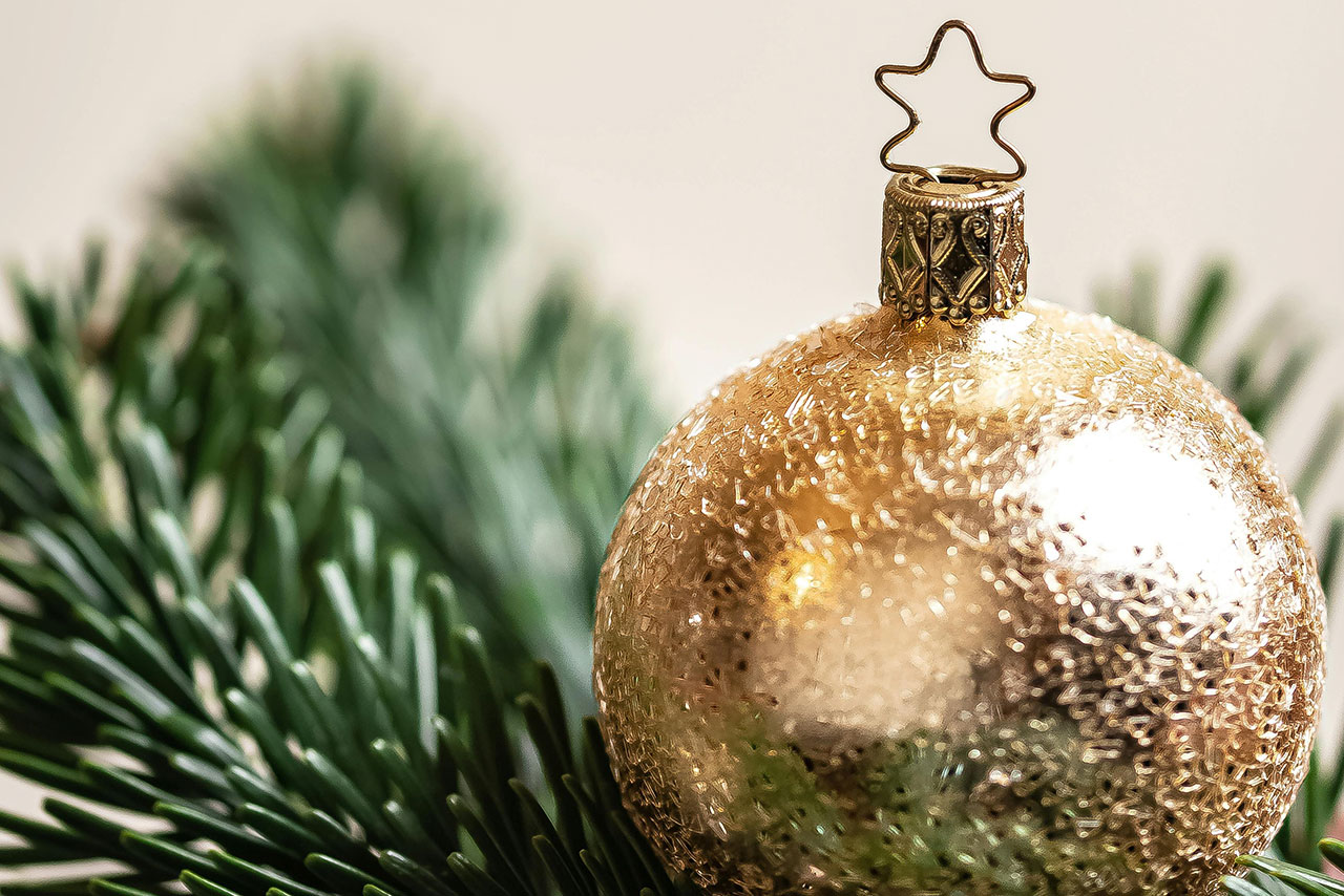 Nahaufnahme eines goldfarbenen Christbaumkugels mit Sternaufhänger vor Tannenzweigen.