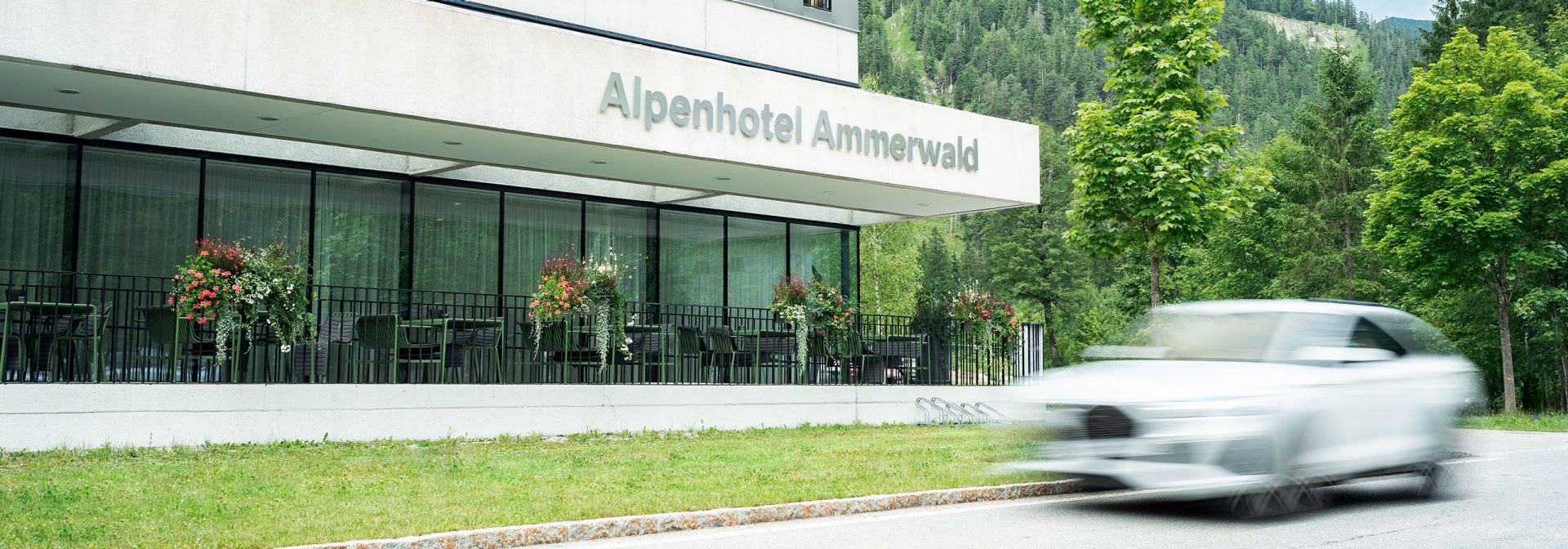 Ein weißes Auto fährt vor dem Hotel.