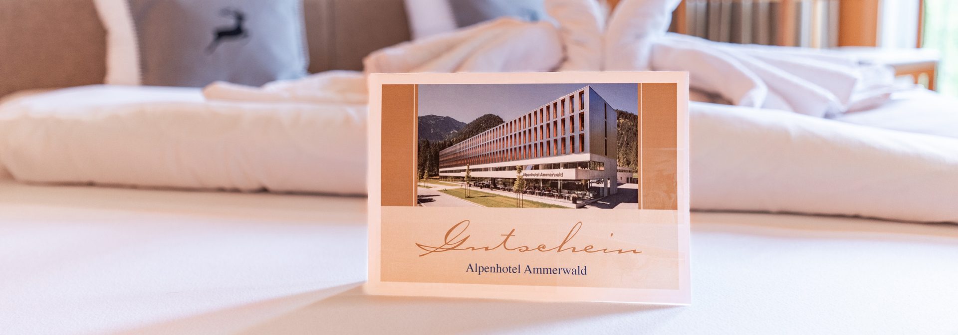 Bild eines Beispiel Gutscheines für das Alpenhotel Ammerwald, auf dem ein Bild vom Hotel abgebildet ist.