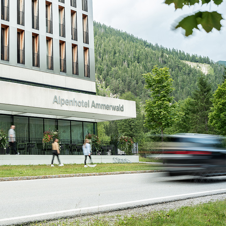 Personen spazieren und Auto fährt vor dem Hotel.