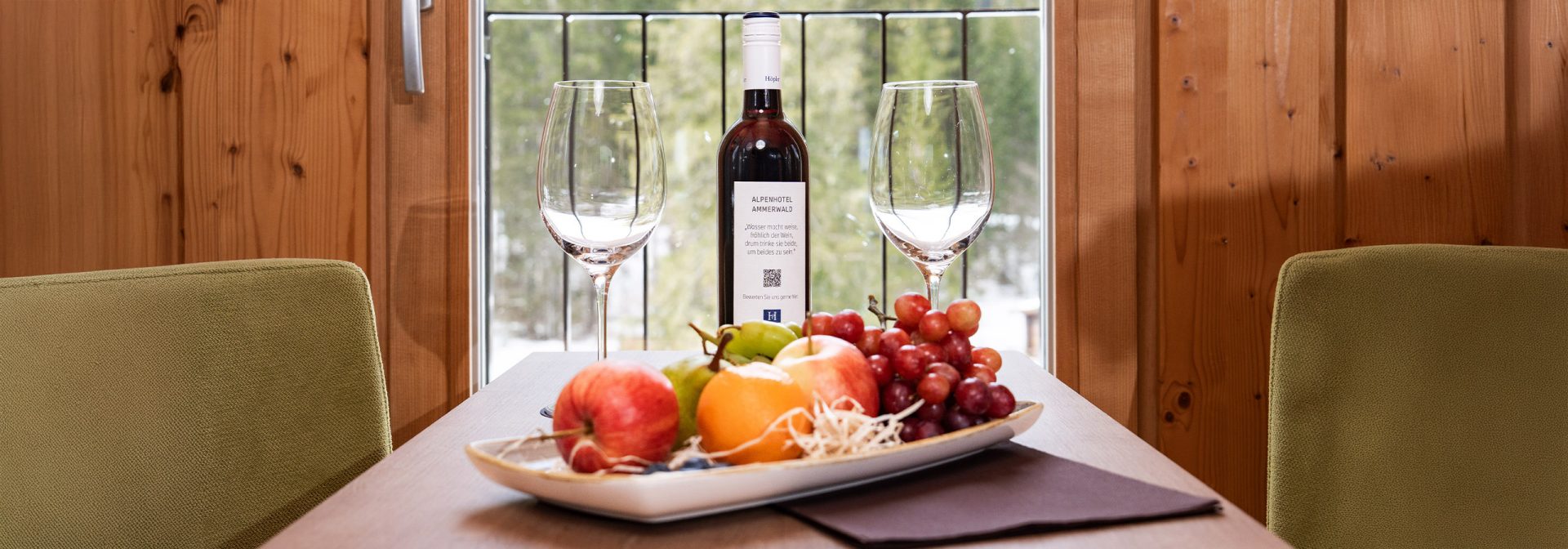 Nahaufname eines gedeckten Tisches mit Früchten, einer Flasche Wein und zwei Gläsern.