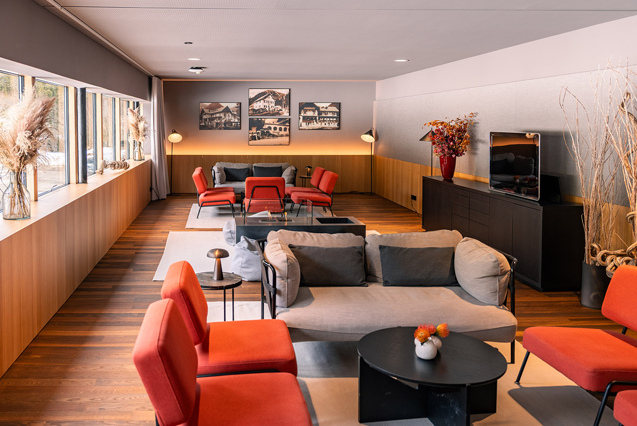 Das Kaminzimmer des Alpenhotel Ammerwalds mit orangenen und grauen Sitzmöbeln und gemütlicher Stimung.