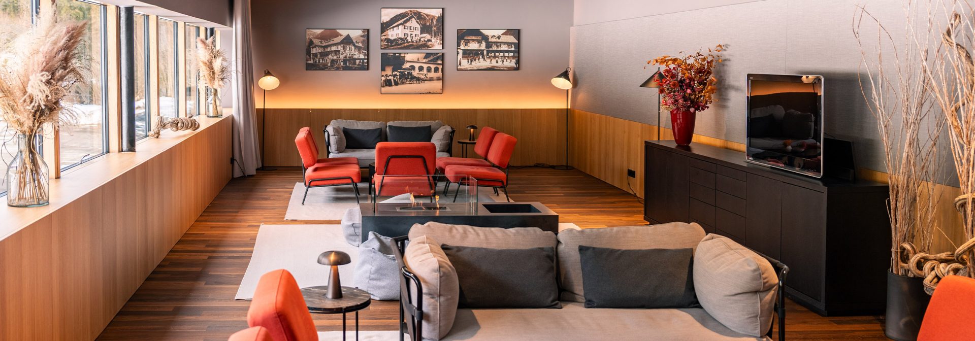 Das Kaminzimmer des Alpenhotel Ammerwalds mit orangenen und grauen Sitzmöbeln und gemütlicher Stimung.