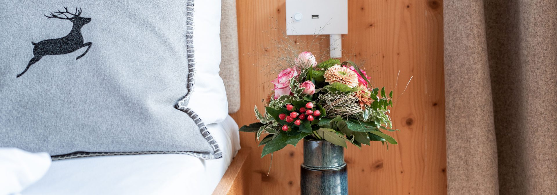 A bouquet of pink flowers in a vase on the table next to a bed