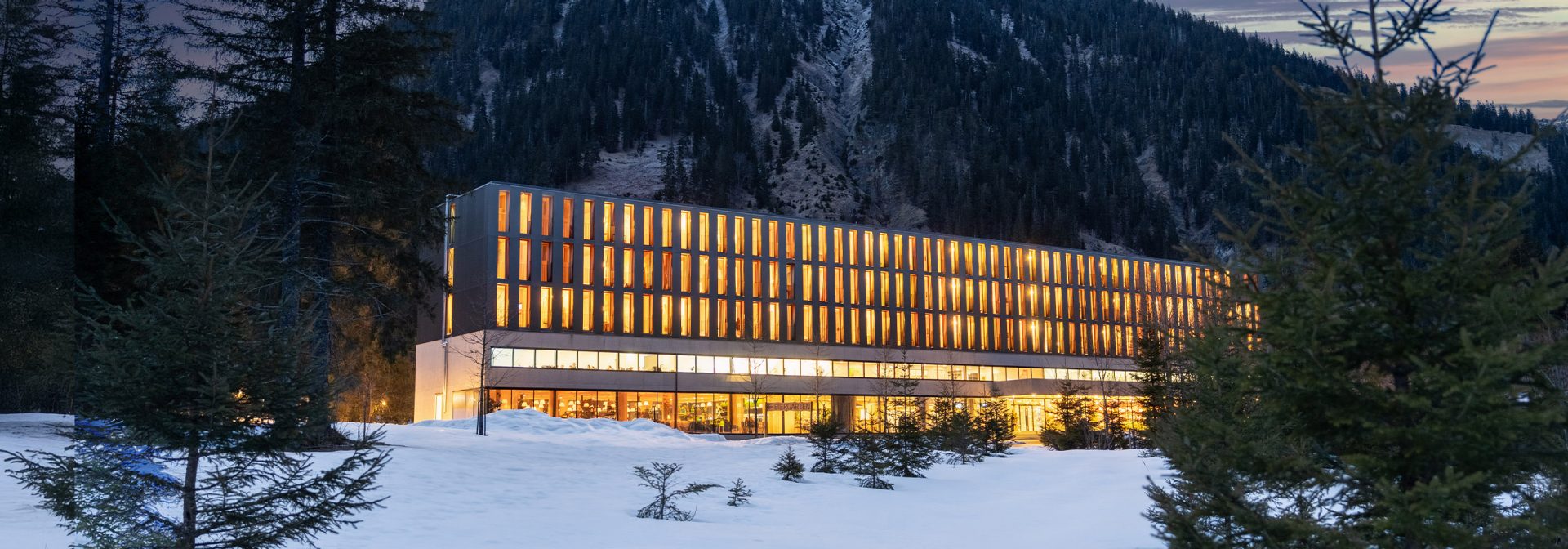A modern hotel with a mountain backdrop, surrounded by snow.