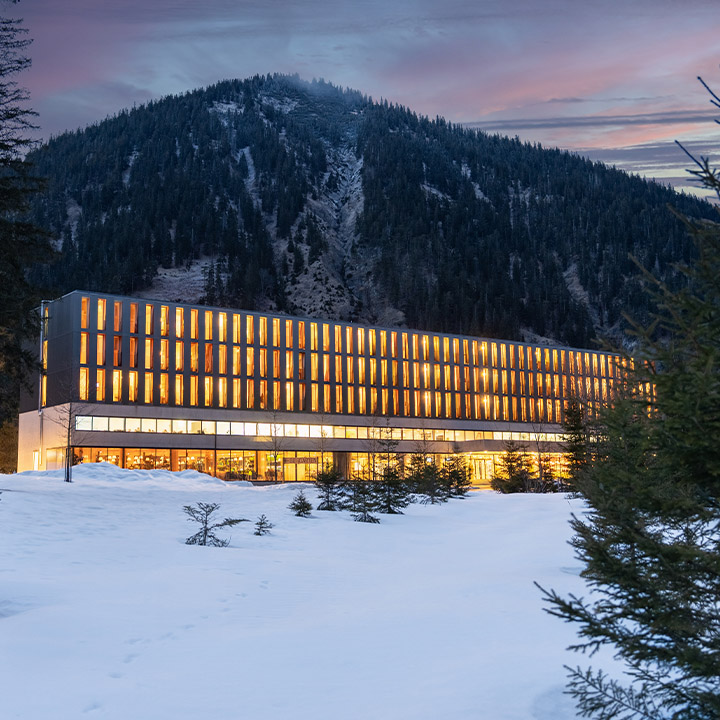 A modern hotel with a mountain backdrop, surrounded by snow.