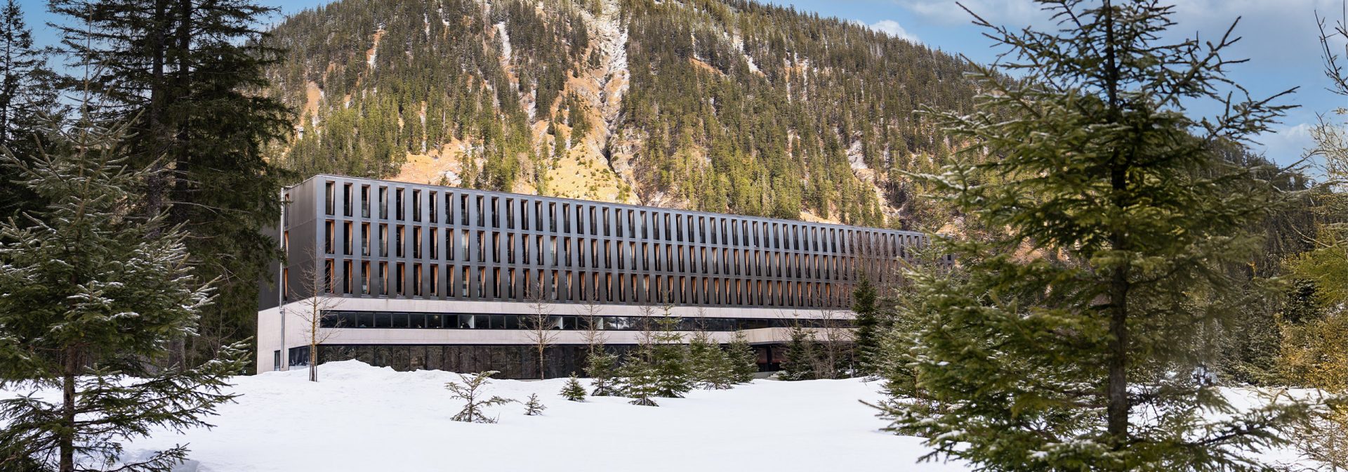 The exterior of a hotel surrounded by snow and pine trees in a mountainous area.