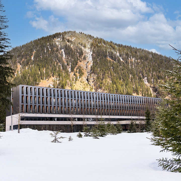 The exterior of a hotel surrounded by snow and pine trees in a mountainous area.
