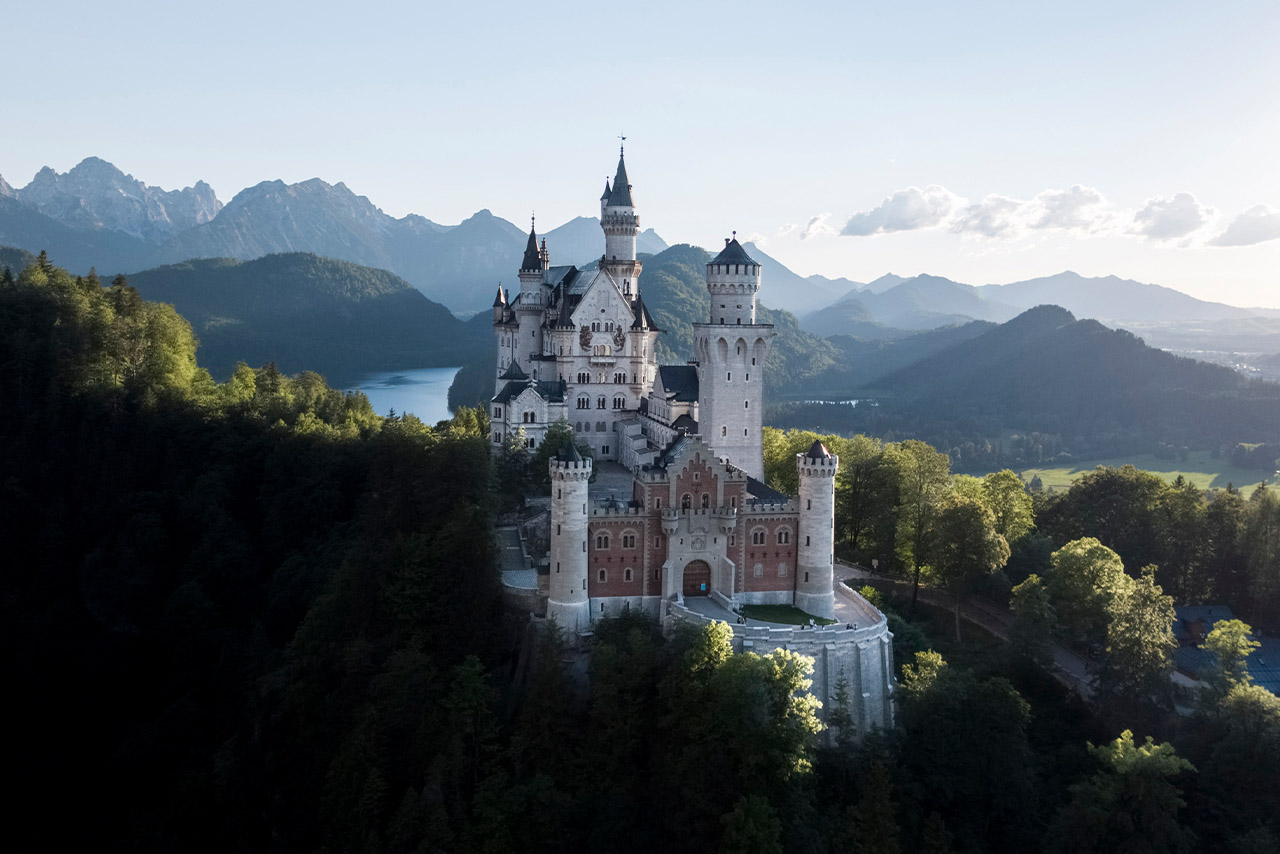 Aerial view of Neuschwanstein Castle surrounded by mountains and forests.