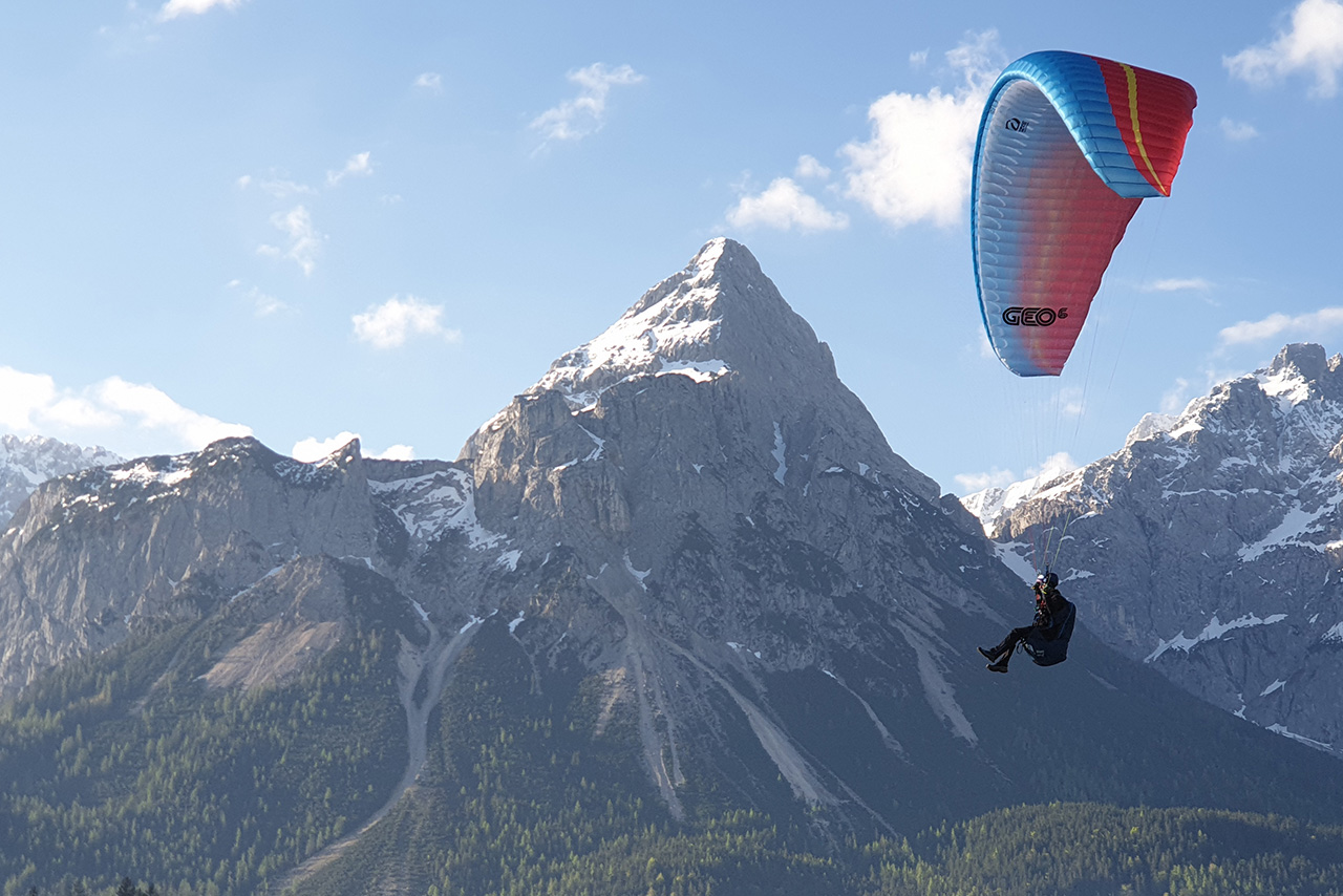 A paraglider soaring above majestic mountains under a clear blue sky.