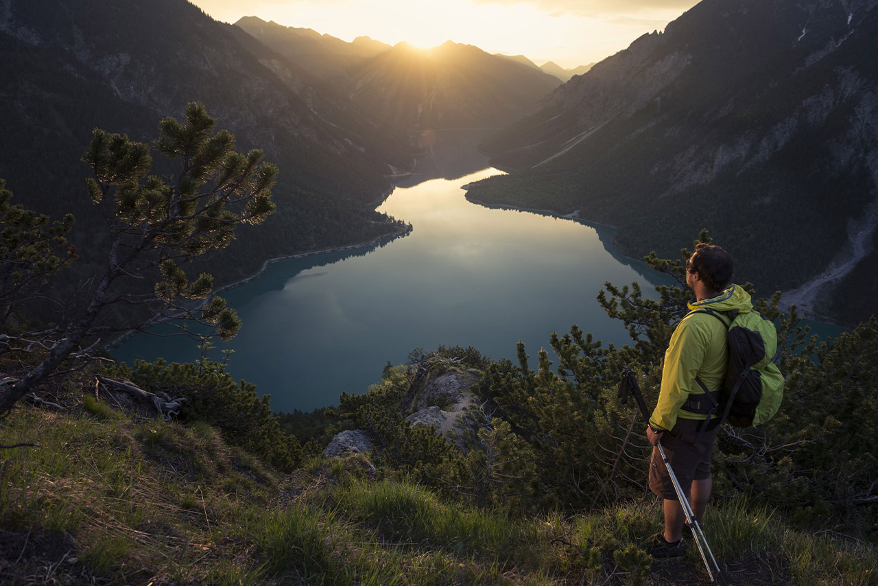 A hiker enjoying a breathtaking sunrise view over a tranquil lake in the mountains.