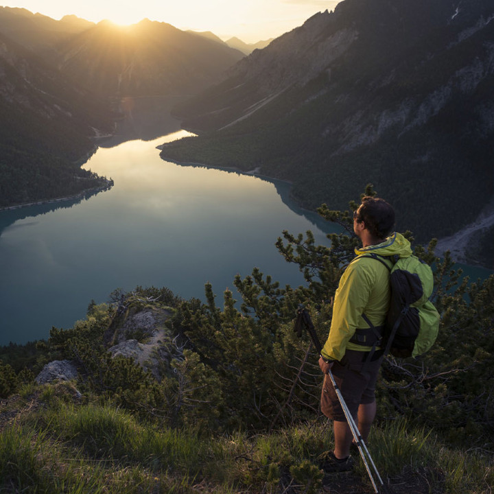 A hiker enjoying a breathtaking sunrise view over a tranquil lake in the mountains.
