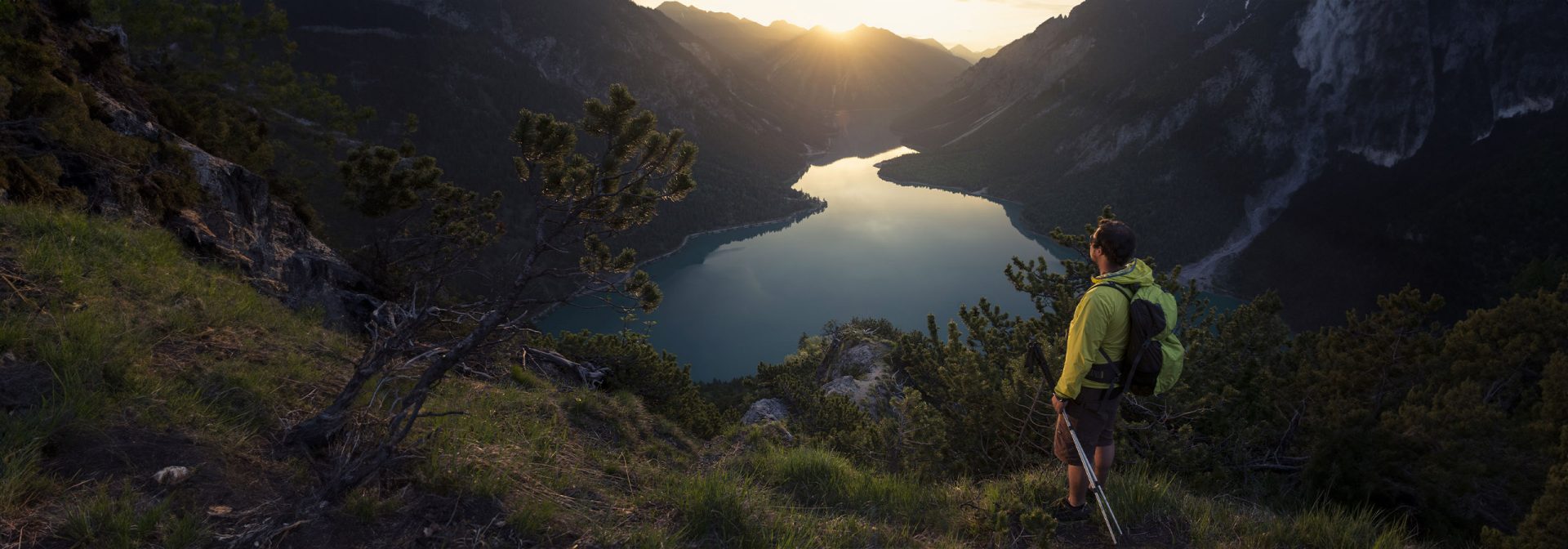 A hiker enjoying a breathtaking sunrise view over a tranquil lake in the mountains.