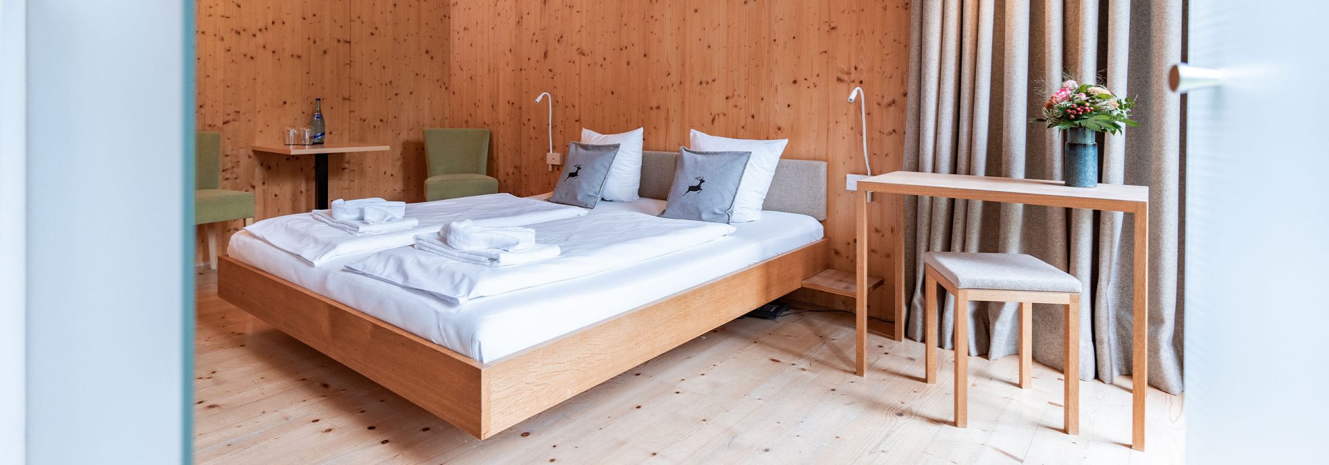 A modern bedroom with wooden walls, a double bed, and a small table with flowers.