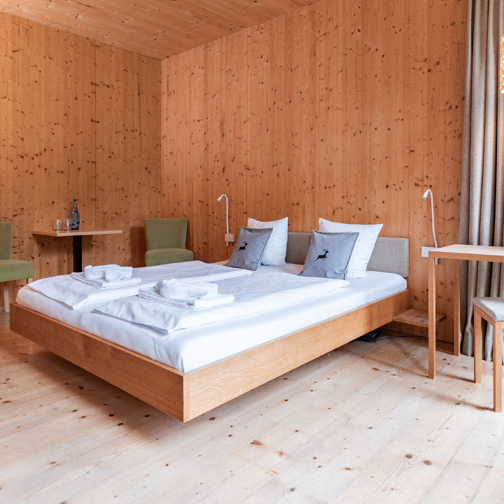 A modern bedroom with wooden walls, a double bed, and a small table with flowers.