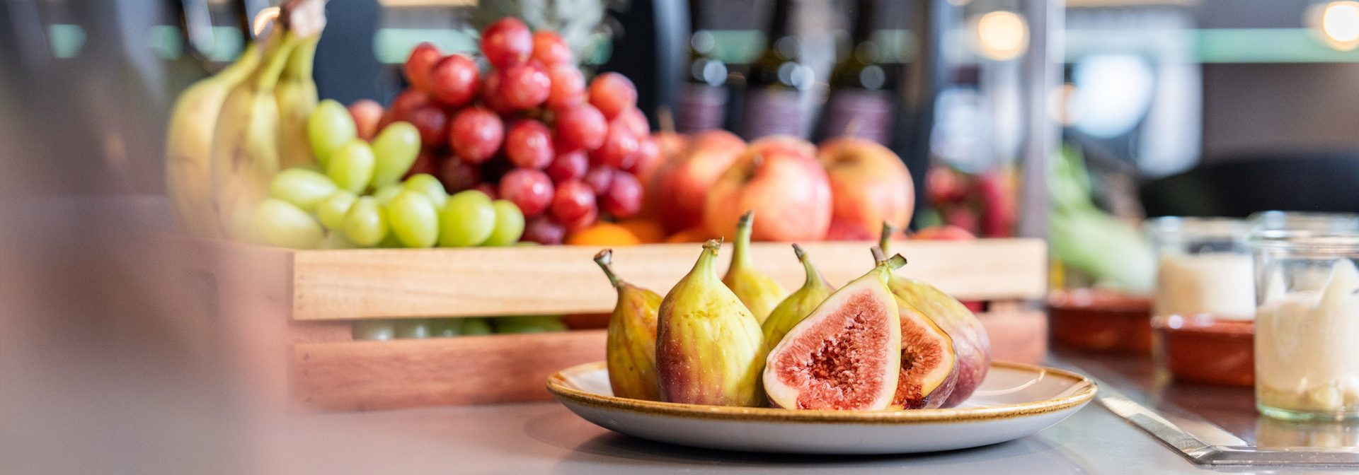 A colorful assortment of fresh fruits including figs, grapes, and apples in a wooden basket.