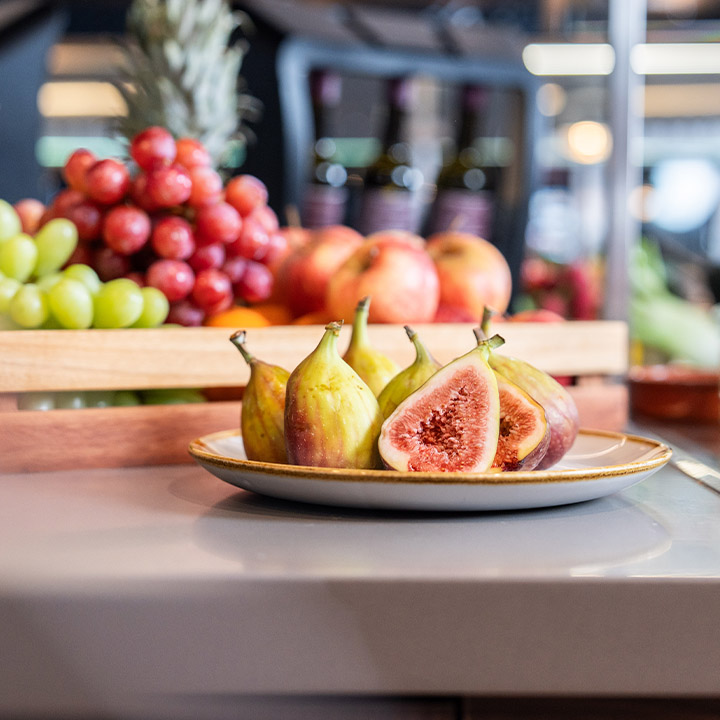 A colorful assortment of fresh fruits including figs, grapes, and apples in a wooden basket.