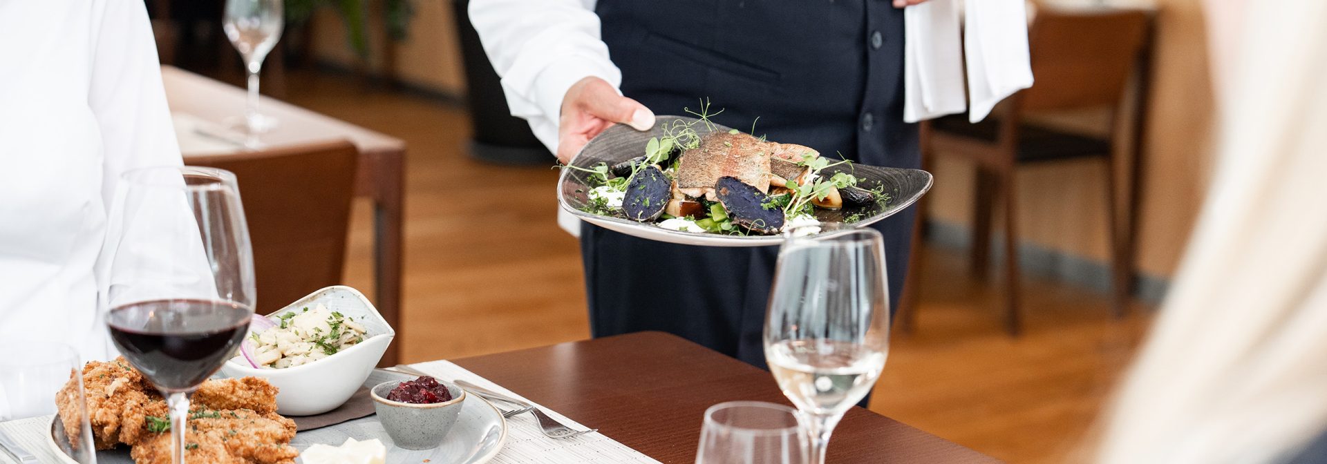 A waiter serving a gourmet dish with vegetables and sauce in a fine dining restaurant.