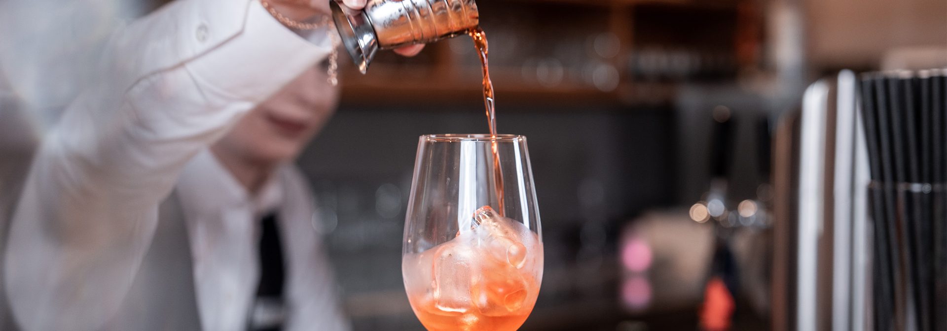 Bartender pouring a cocktail into a glass with ice.