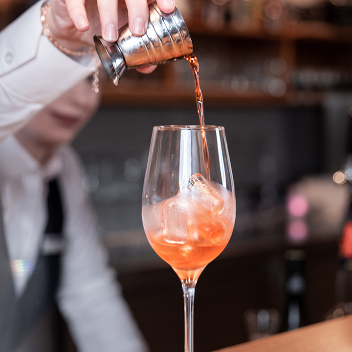 Bartender pouring a cocktail into a glass with ice.