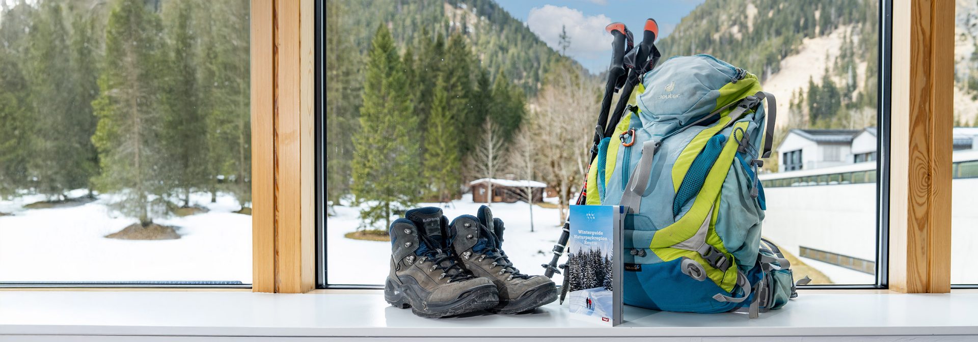 Hiking gear including a backpack and boots by the window with a scenic view.