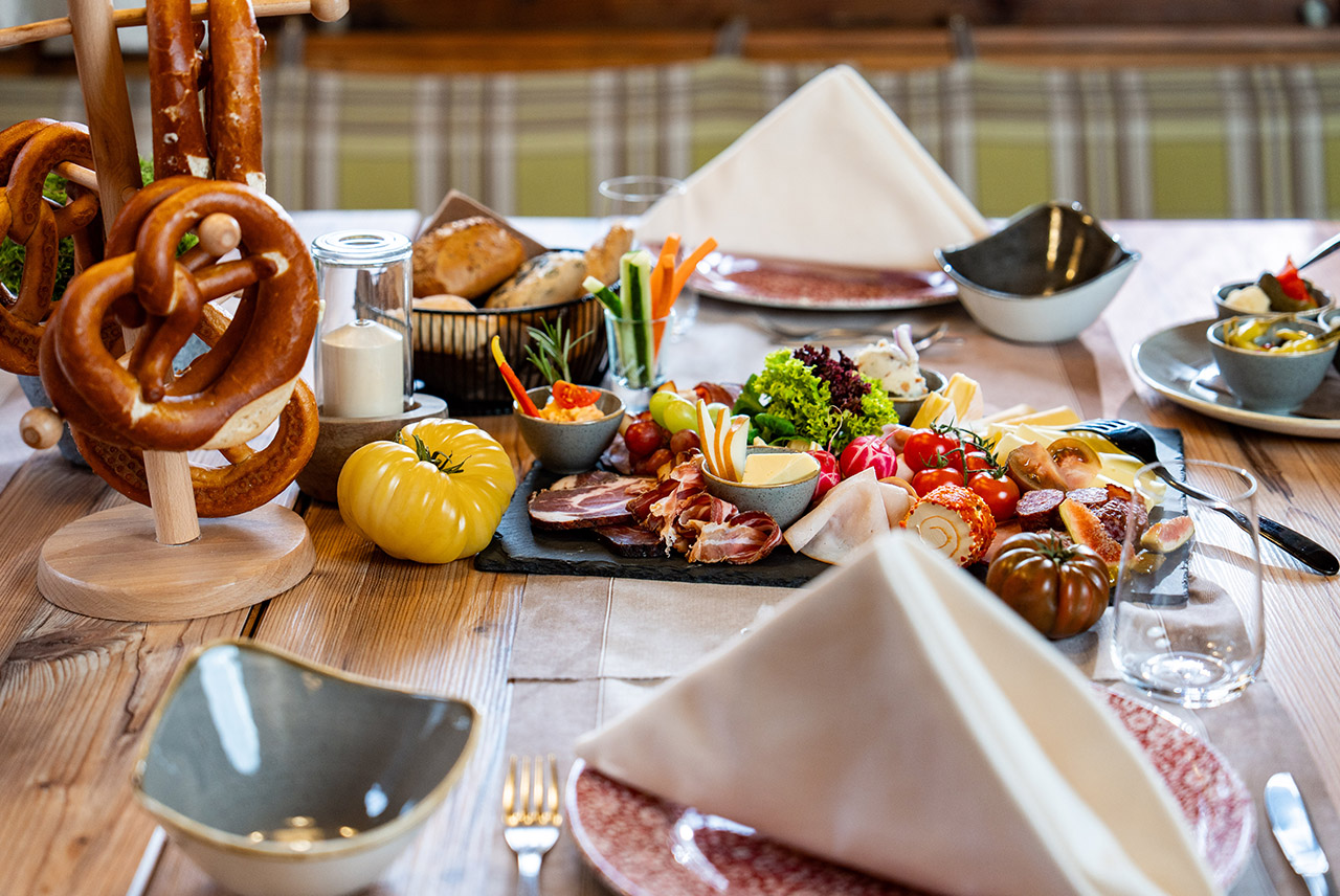 Nahaufname eines gedeckten Tisches mit Früchten, einer Brotzeitplatte, Brezen und Gläsern.