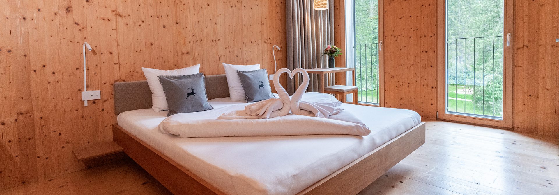 A cozy wooden bedroom featuring a heart-shaped towel arrangement on a neatly made bed.