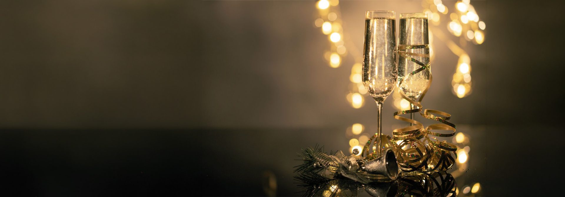 Two champagne glasses on a table with Christmas decorations and string lights in the background