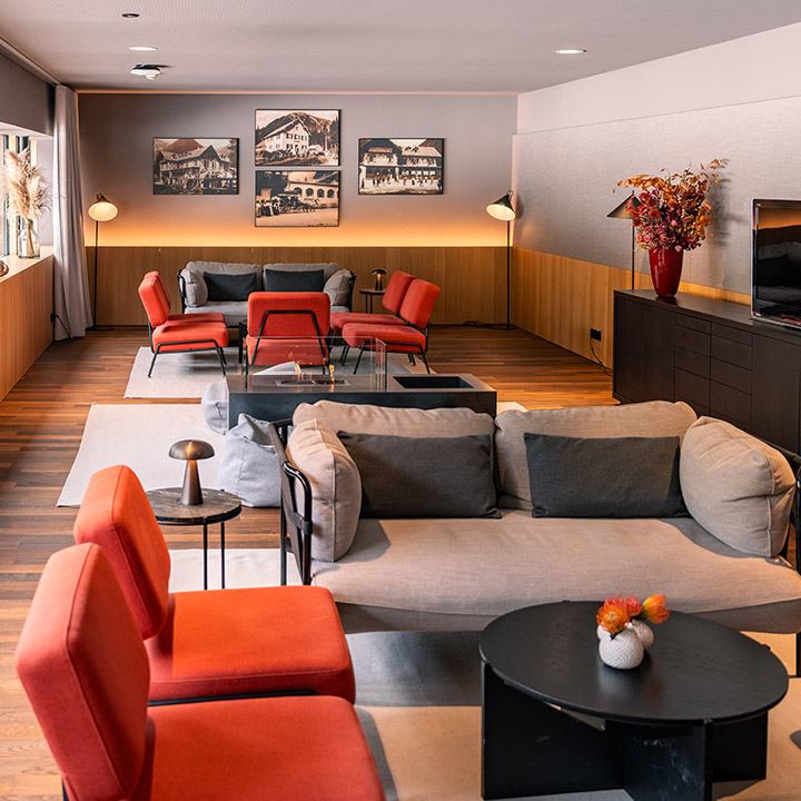 Das Kaminzimmer des Alpenhotel Ammerwalds mit orangenen und grauen Sitzmöbeln und gemütlicher Stimung.